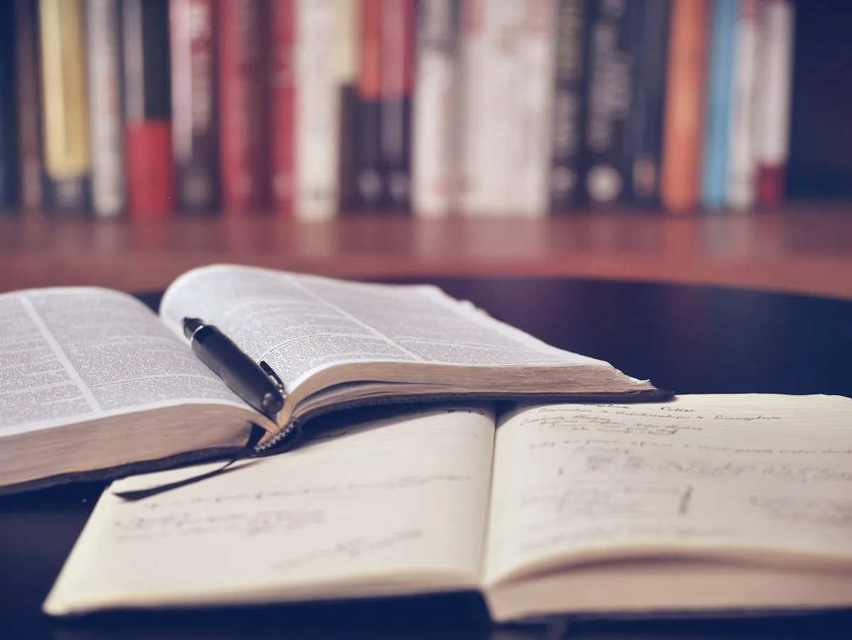 Open books and notes on a desk in front of a bookshelf